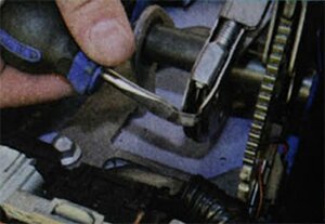 Отверткой отогните фиксатор оболочки переднего троса привода стояночного тормоза